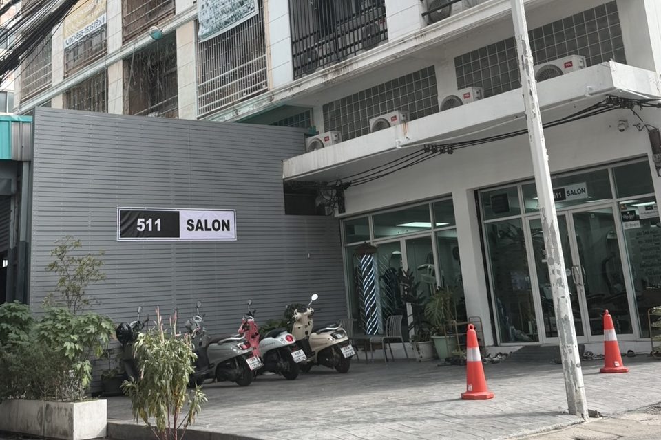 หน้าร้าน 511 SALON ป้ายชื่อร้านสีขาวดำบนผนังสีเทา ถัดไปเป็นกระจกหน้าร้านและทางเข้า มีมอเตอร์ไซค์จอดอยู่ริมทางเดิน