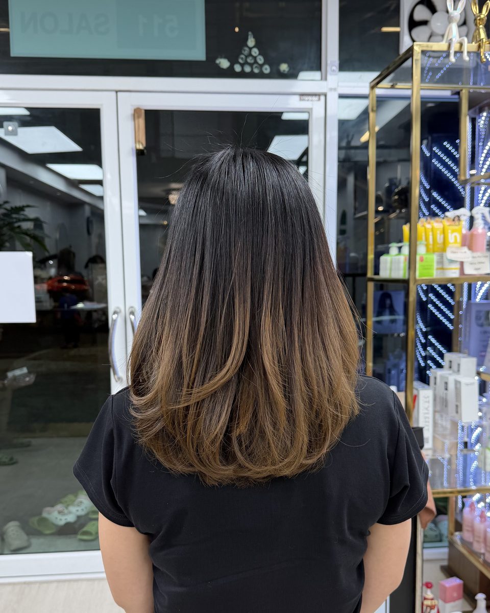 ผมยาวประบ่าไล่โทนจากโคนสีเข้มไปปลายสีคาราเมล ตัดเลเยอร์ ถ่ายที่หน้ากระจกร้าน